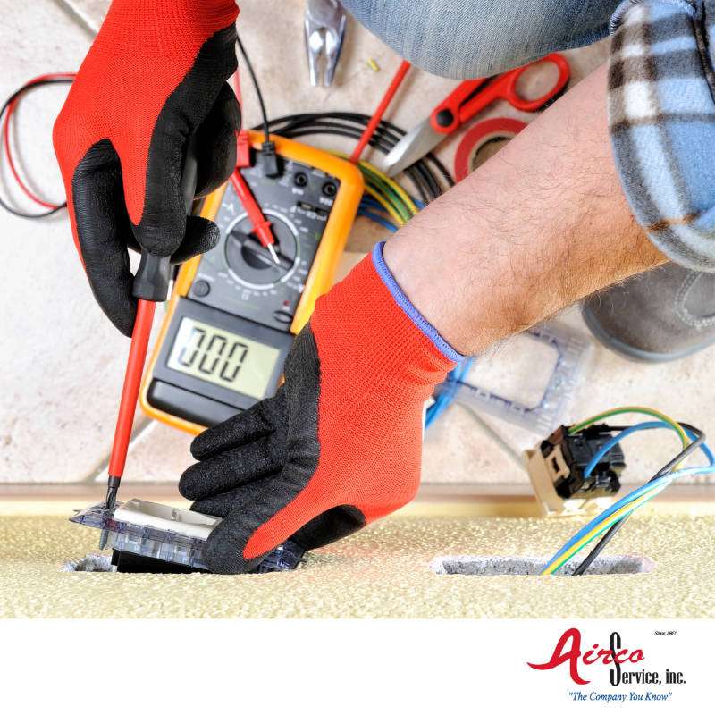Electrician working on outlet, Airco Service logo in bottom right